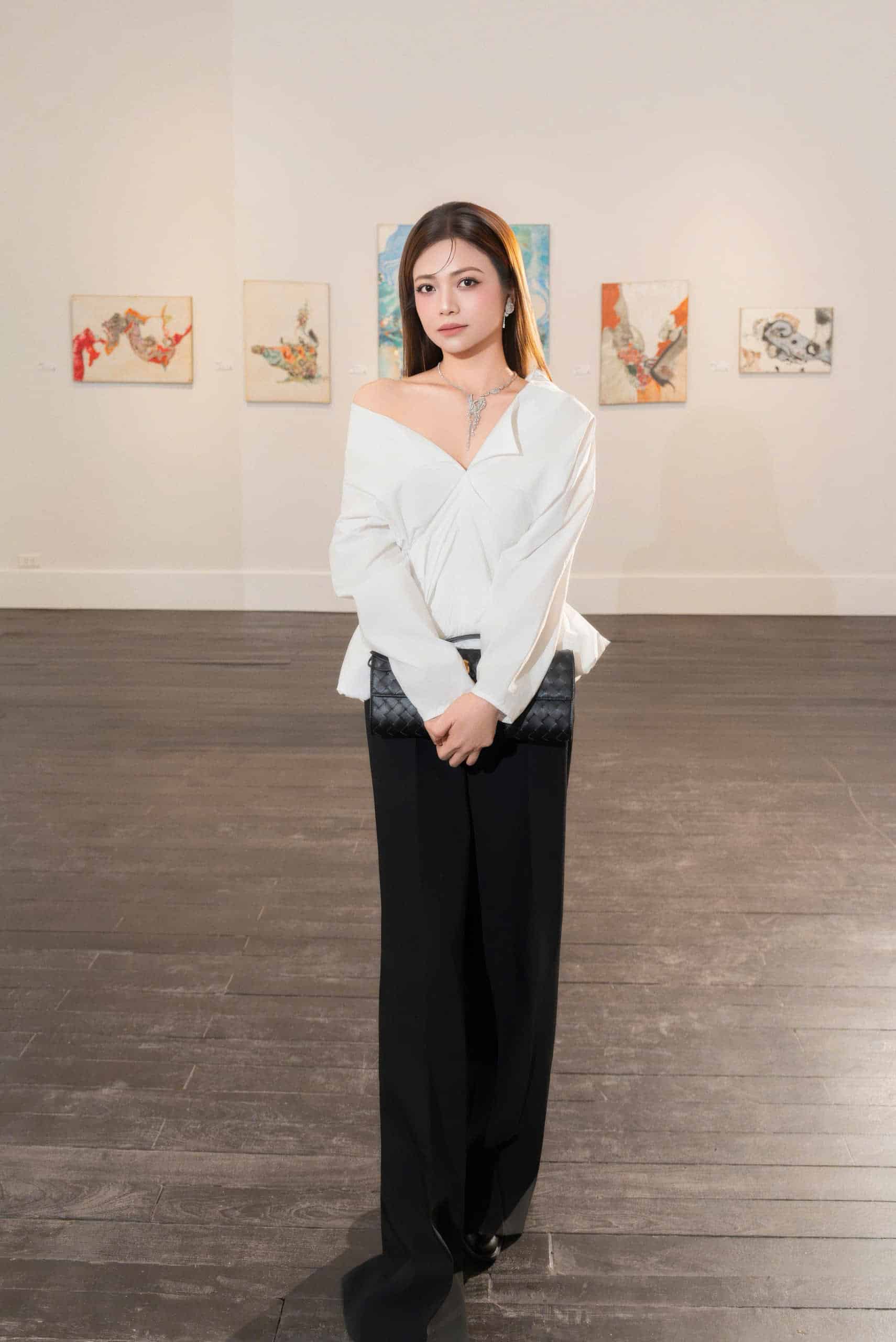 NSƯT Kiều Anh mặc áo trắng và quần đen đứng giữa phòng triển lãm tranh